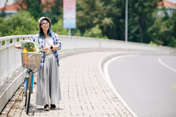 Mooi mooi jong aziatisch vrouw in hoed lopen langs weg met fiets - Foto, afbeelding