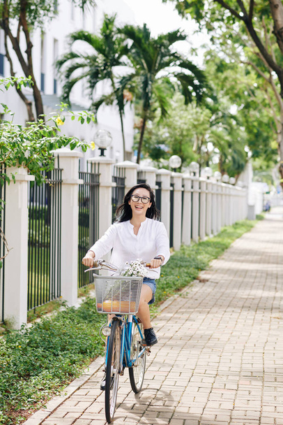 Boldog fiatal kínai nő kerékpározik végig a város utcáján - Fotó, kép