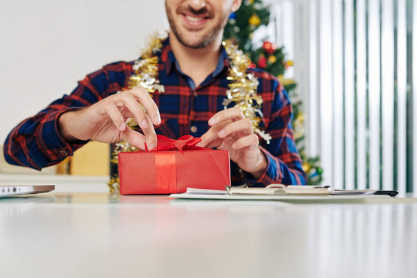 Excited smiling entrepreneur opening Christmas present at office desk - Photo, image