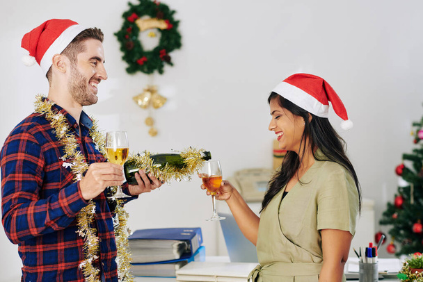 Веселые молодые бизнесмены пьют шампанское во время празднования Рождества в офисе - Фото, изображение
