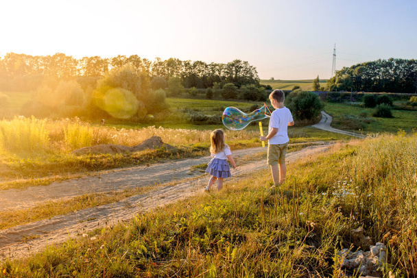 Boldog gyerekek játszanak szappanbuborékokkal a nyári természetben. Buborékok a naplementében - Fotó, kép