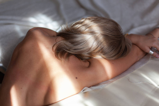 cropped image of naked female back with hands with white sheet background and sunlight - Photo, Image