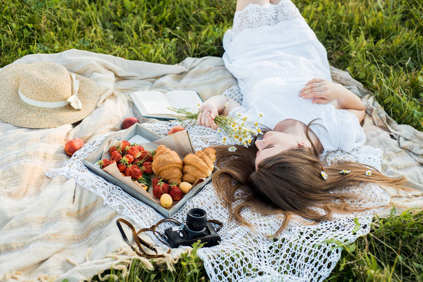 Field in daisies, a bouquet of flowers.Summer picnic by the sea. basket for a picnic with with buns, apples and juice. girl on a picnic lies and reads a book - Foto, Imagen