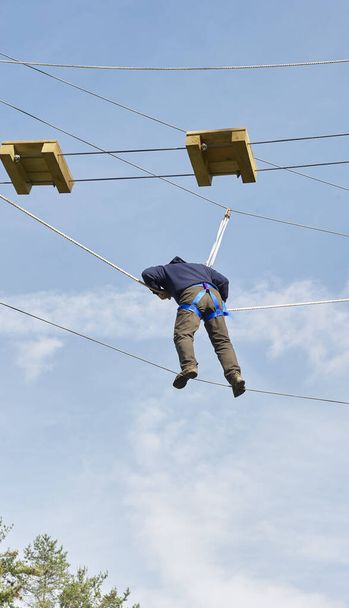 high ropes/challenge course.  participant walking guide wire while safety roped in. - Photo, Image