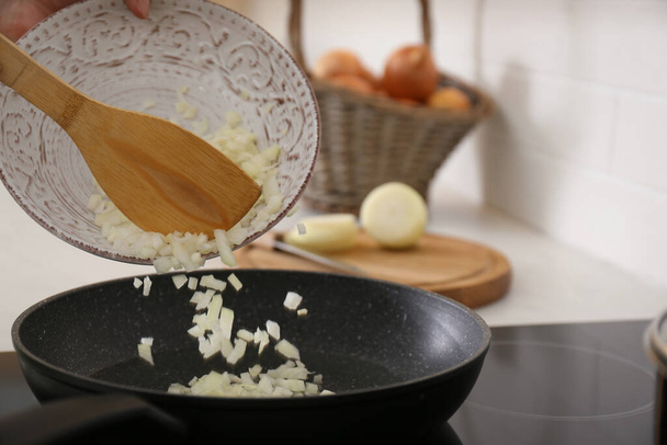 Woman pouring chopped onion into frying pan in kitchen, closeup - Foto, immagini