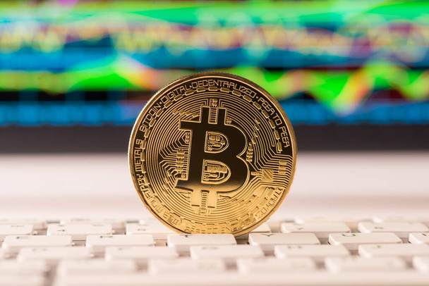 Close up photo of golden bitcoin standing on white keyboard with digital chart graph on the backdrop - Photo, Image
