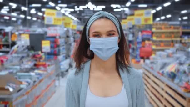 Nuori nainen lääketieteellisessä naamiossa kävelemässä supermarketissa  - Materiaali, video
