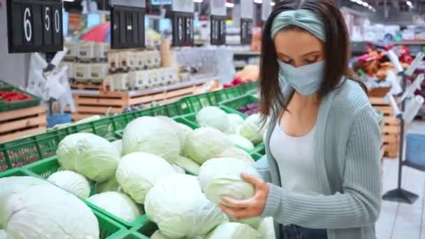 vrouw met medisch masker zet kool in winkelwagen - Video