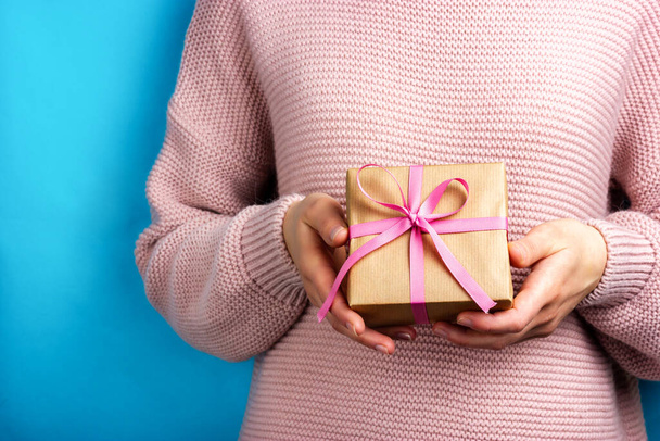 A girl in a pink sweater holds a gift wrapped in craft paper. - Foto, immagini