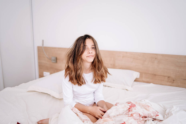 The girl is in bed in the morning, rejoices at waking up with a good mood.Portrait pretty young girl on bed in modern apartment in the morning. She keeps eyes closed and looks satisfied - 写真・画像