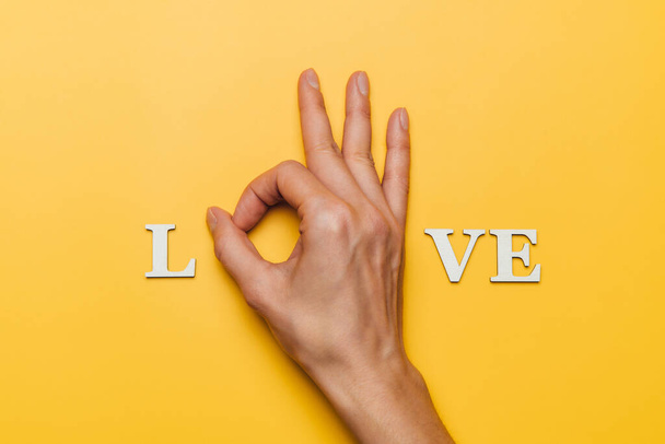 Flat lay of woman hand as part of word love on yellow background - Фото, изображение