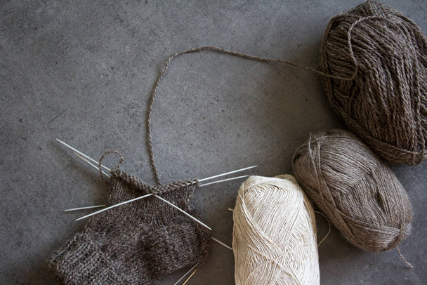 Cozy knitting. Brown wool socks on grey background. Needle work in progress. Natural sheep wool sock close up photo. - Photo, Image