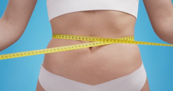 Close up tiro de mulher medindo sua cintura com fita métrica, fundo do estúdio azul - Filmagem, Vídeo