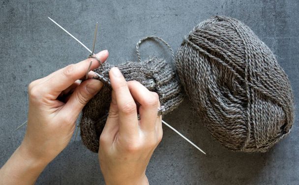Les mains de femme tenant des aiguilles à tricoter ferment la photo sur fond gris avec de l'espace de copie. Tricoter des chaussettes chaudes.  - Photo, image