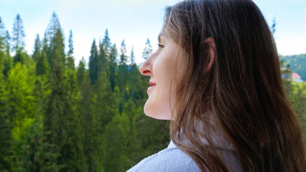 Mladá uvolněná žena v županu stojí na balkóně hotelového pokoje a dívá se na hory a les. Koncept cestovního ruchu a dovolené v horách v létě - Fotografie, Obrázek