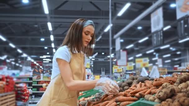 jonge merchandiser in schort verzamelen wortelen in supermarkt  - Video