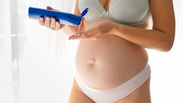 Close-up de mulher grávida em lingerie aplicando creme hidratante loção ou formiga estrias na barriga remo e corpo. Conceito de beleza, gravidez e cuidados de saúde. - Foto, Imagem