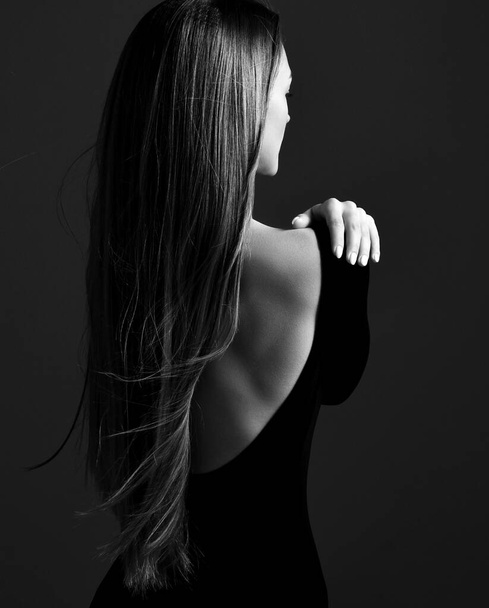 Young pretty woman model standing backwards in dress with open back and showing her gorgeous silky long straight hair - Foto, Imagen