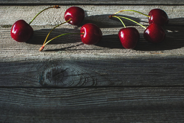 cherries arranged in a row on wooden table in a streak of light - Zdjęcie, obraz