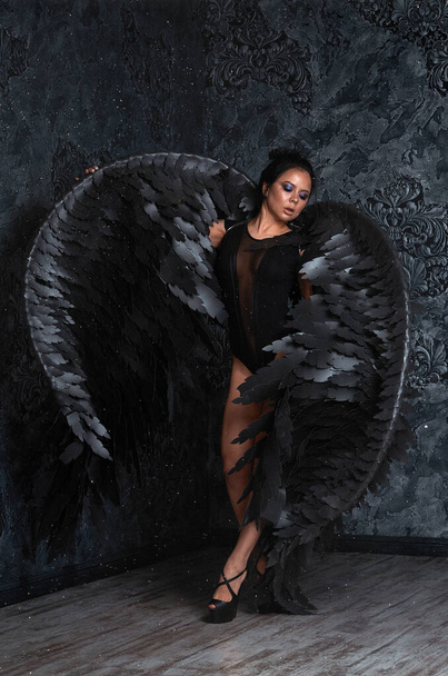 dziewczyna z czarnym aniołem skrzydła w ciemnym pokoju. - Zdjęcie, obraz
