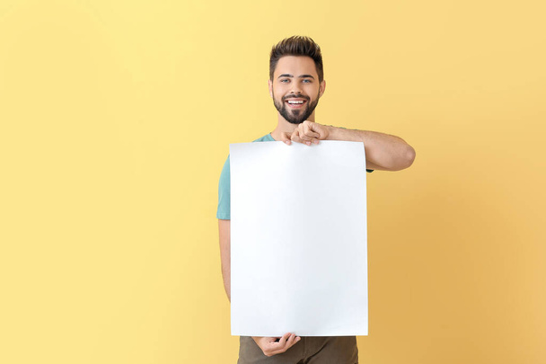 Jeune homme avec feuille de papier vierge sur fond de couleur - Photo, image