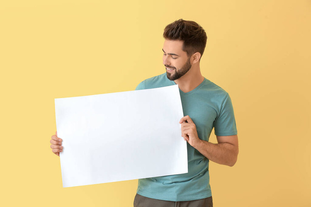 Junger Mann mit leerem Blatt Papier auf farbigem Hintergrund - Foto, Bild