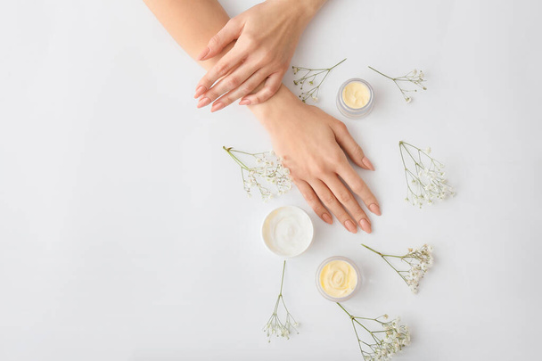 Female hands with cream and beautiful flowers on light background - Foto, Bild