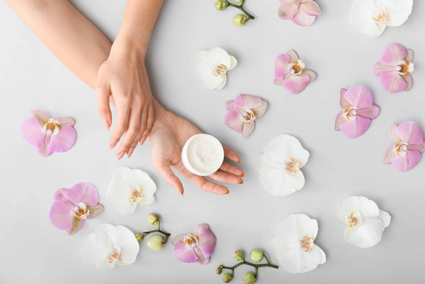 Female hands with cream and beautiful flowers on light background - Valokuva, kuva