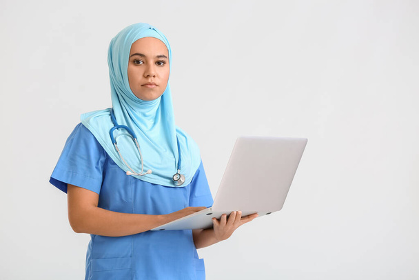 Portrait of female Muslim doctor with laptop on light background - 写真・画像