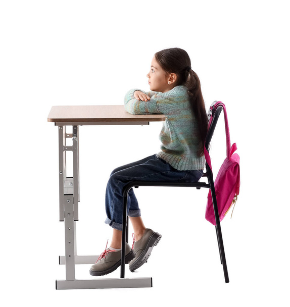 Klein schoolmeisje met slechte houding zitten aan het bureau tegen witte achtergrond - Foto, afbeelding