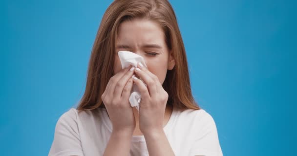 Studio portret van jonge zieke dame blaast haar neus, blauwe achtergrond, slow motion - Video
