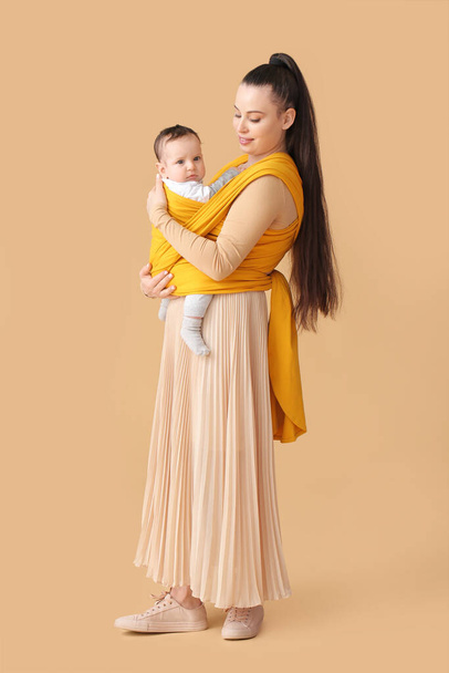 Young mother with little baby in sling on light background - Photo, Image