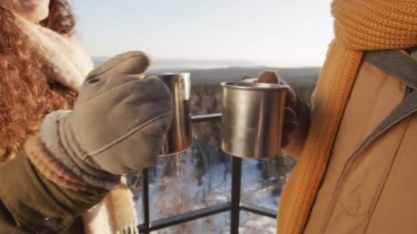 Primer plano de pareja irreconocible de pie fuera en el día de invierno soleado tazas de metal tintineo con la bebida caliente calentamiento - Metraje, vídeo