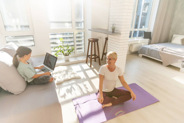 Zeit für Yoga. Attraktive junge Frau beim Training und Sitzen in Yoga-Lotusposition, während sie zu Hause ruht - Foto, Bild
