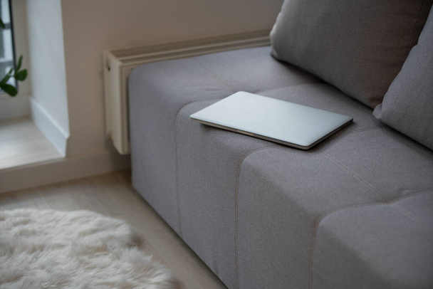 Nahaufnahme eines geschlossenen Laptops, der auf einem grauen Sofa liegt - Foto, Bild