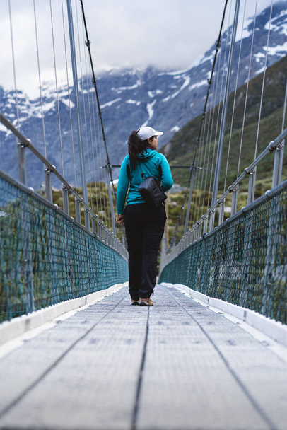 Молодая женщина, идущая по подвесному мосту в национальном парке Маунт-Кук. Гукер Вэлли Трек. Новая Зеландия - Фото, изображение
