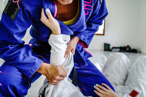 Grips from the guard in brazilian jiu jitsu bjj or judo training sparring two female women athletes fighters drilling techniques for the competition advanced guard holding kimono gi for self-defense - Photo, Image