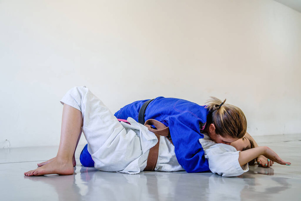 Zijbesturing 100 kilo positie, amerikaanse onderwerping judo bjj braziliaanse jiu-jitsu training sparren twee vrouwelijke vechters in training dragen kimono - Foto, afbeelding