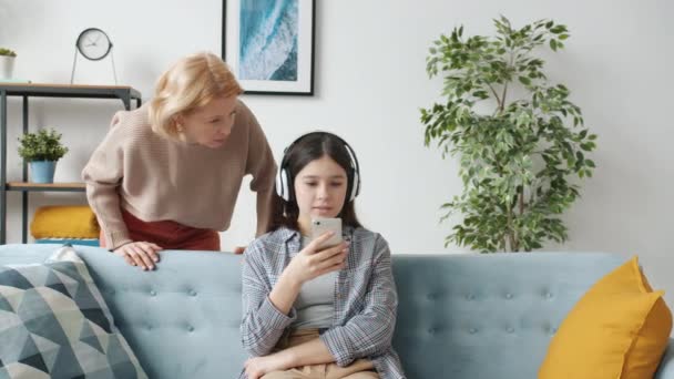 Offended teenager listening to music and using smartphone ignoring angry mother - Imágenes, Vídeo