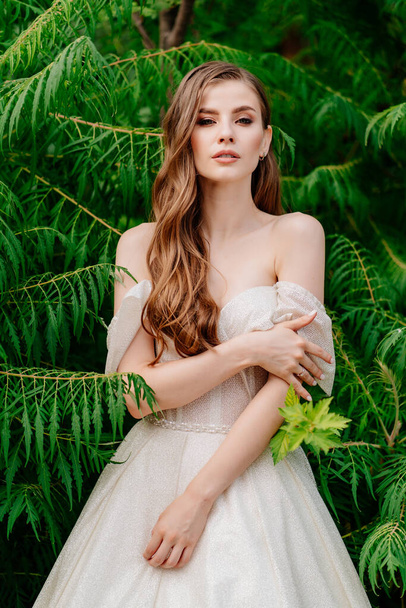 beautiful woman in a white dress posing in against of green leaves. - 写真・画像
