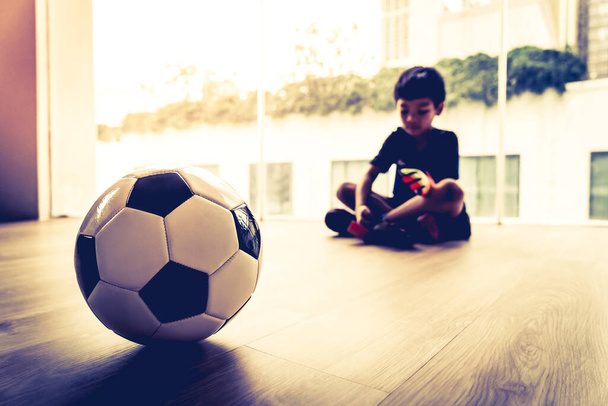 Little Football goalkeeper boy is sitting and relaxing with soccer ball on the foreground. - Photo, Image