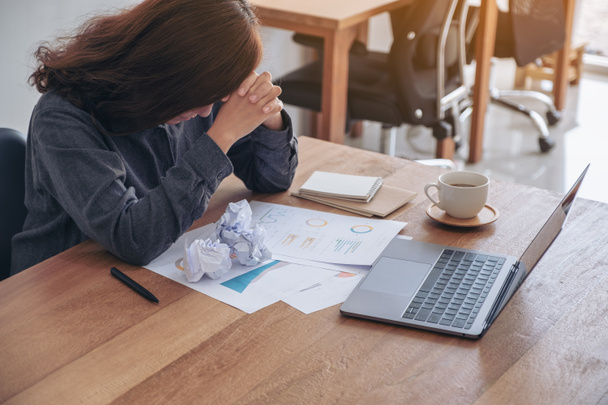 Деловая женщина, работающая с чувством разочарования и стресса из-за испорченных бумаг и ноутбука на столе в офисе - Фото, изображение