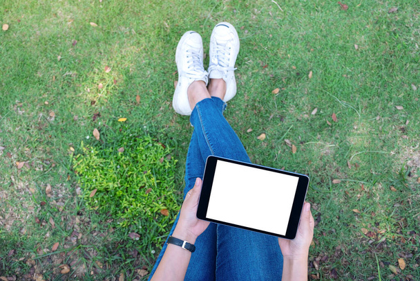 Top view mockup image of a woman holding and using black tablet pc with blank white desktop screen while sitting in the outdoors - Foto, Bild