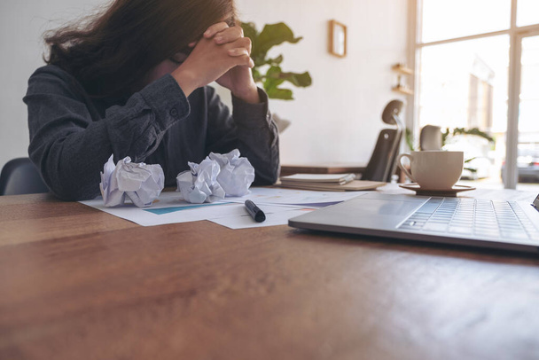 Eine Geschäftsfrau, die frustriert und gestresst mit vermasselten Papieren und Laptop auf dem Tisch im Büro arbeitet - Foto, Bild