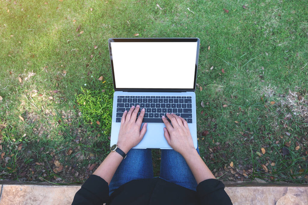 Вид сверху макет изображения женщины, использующей и печатающей на ноутбуке с чистым белым экраном, сидящей на открытом воздухе с природным фоном - Фото, изображение