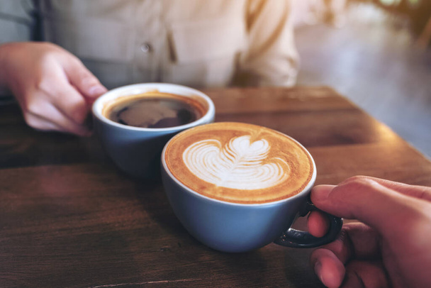 Immagine ravvicinata di un uomo e una donna che tintinnano tazze di caffè blu su un tavolo di legno nel caffè - Foto, immagini