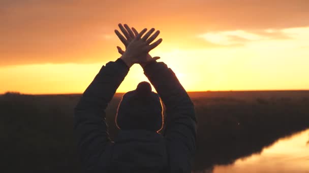 Een man zwaait met zijn handen bij zonsondergang en vraagt om hulp, gered van het gevaar te verdwalen. Man in de schittering van de zon springt. Man bij zonsopgang op kampeervakantie of alleen op reis - Video