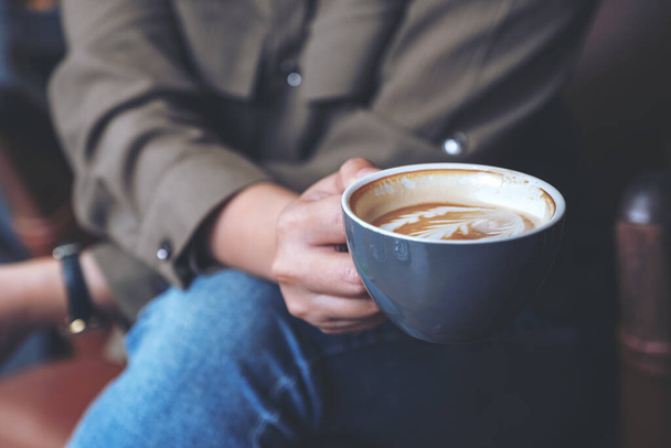 Imagen de cerca de la mano de una mujer sosteniendo y bebiendo café con leche caliente mientras está sentada en la cafetería - Foto, imagen