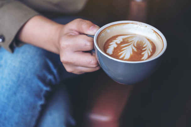 Zbliżenie obraz dłoni kobiety trzymającej i pijącej gorącą kawę latte siedzącej w kawiarni - Zdjęcie, obraz