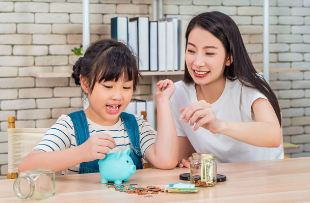 Asiática madre está enseñando a su hija sobre el ahorro financiero y la gestión del dinero utilizando alcancía y ahorro tarro. - Foto, Imagen